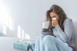 Sick Woman Blowing Nose And Holding Mug