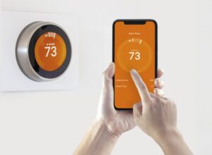 Orange Smart Thermostat On Wall Connected To Smart Phone App